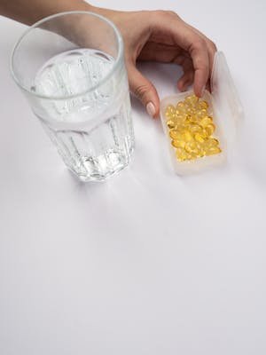 Close-up of a hand reaching for vitamin capsules next to a glass of water.