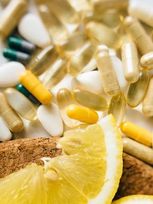Close-up of assorted vitamins, supplements, and lemon slices on a cork surface.